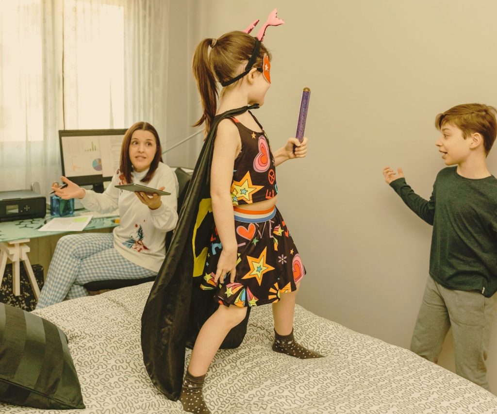 Maman en télétravail sur son ordinateur pendant que ses deux enfants jouent à côté, illustrant la vie de maman freelance